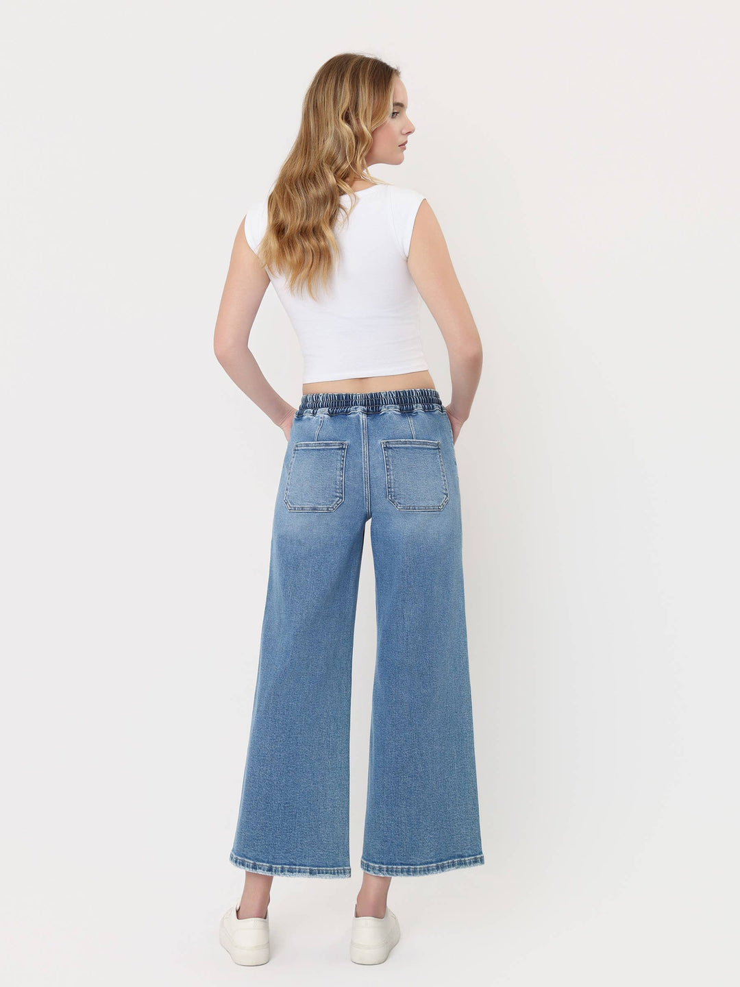 Light-wash cropped wide-leg jeans with a high-rise drawstring waistband, oversized front patch pockets, and finished hem, styled with a white crop top and white sneakers.