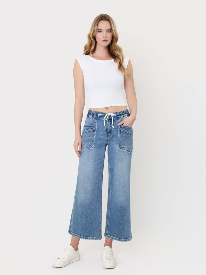 Light-wash cropped wide-leg jeans with a high-rise drawstring waistband, oversized front patch pockets, and finished hem, styled with a white crop top and white sneakers.
