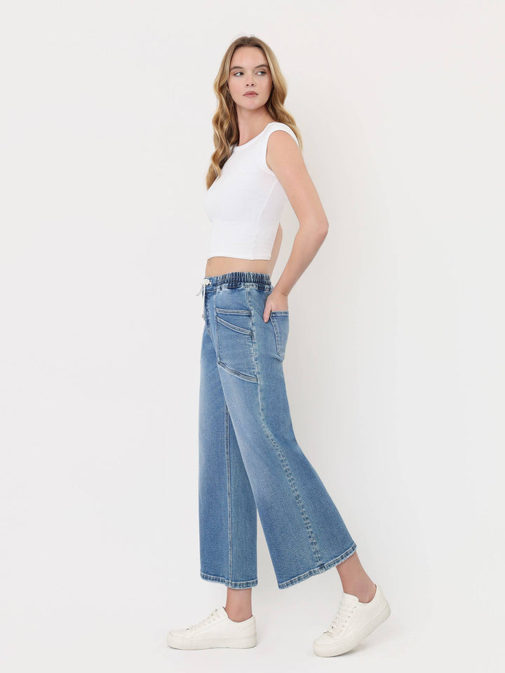 Light-wash cropped wide-leg jeans with a high-rise drawstring waistband, oversized front patch pockets, and finished hem, styled with a white crop top and white sneakers.