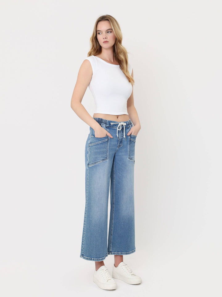 Light-wash cropped wide-leg jeans with a high-rise drawstring waistband, oversized front patch pockets, and finished hem, styled with a white crop top and white sneakers.