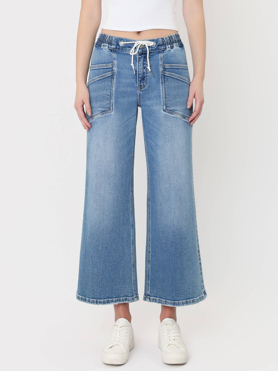 Light-wash cropped wide-leg jeans with a high-rise drawstring waistband, oversized front patch pockets, and finished hem, styled with a white crop top and white sneakers.
