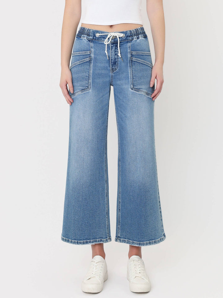 Light-wash cropped wide-leg jeans with a high-rise drawstring waistband, oversized front patch pockets, and finished hem, styled with a white crop top and white sneakers.