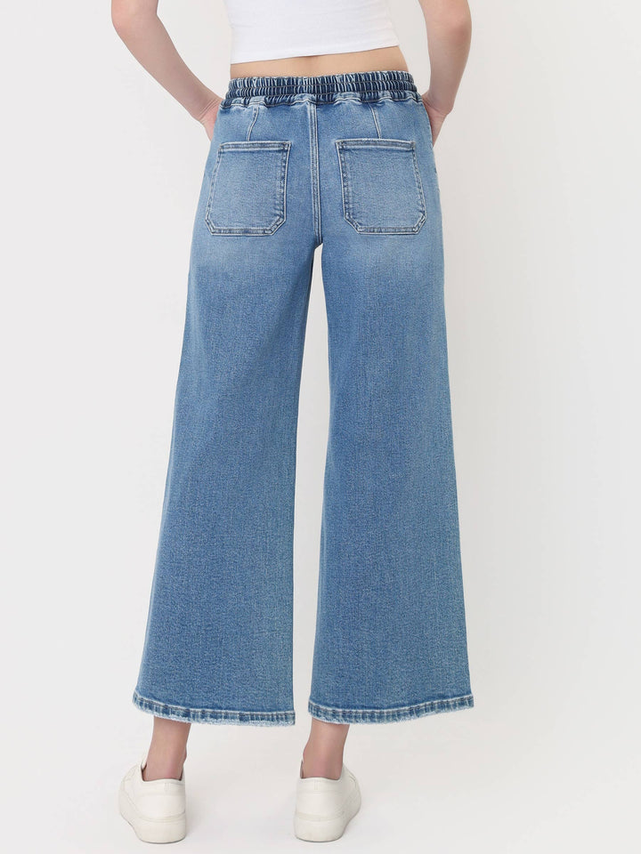 Light-wash cropped wide-leg jeans with a high-rise drawstring waistband, oversized front patch pockets, and finished hem, styled with a white crop top and white sneakers.