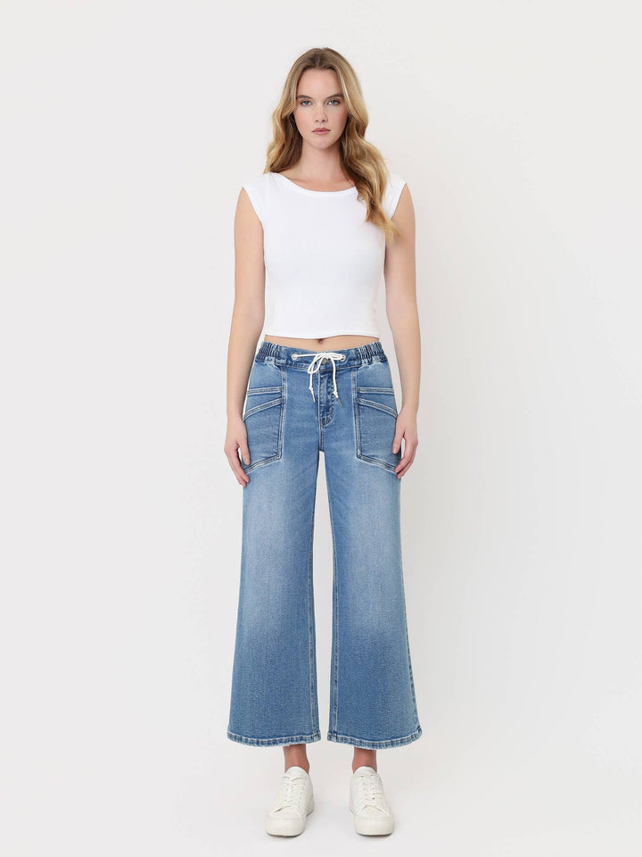 Light-wash cropped wide-leg jeans with a high-rise drawstring waistband, oversized front patch pockets, and finished hem, styled with a white crop top and white sneakers.
